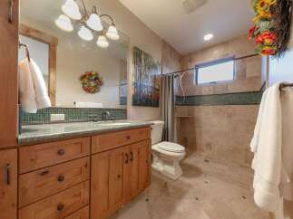 This charming bathroom features a custom wood vanity with a granite countertop, complemented by a tiled backsplash and a large mirror.