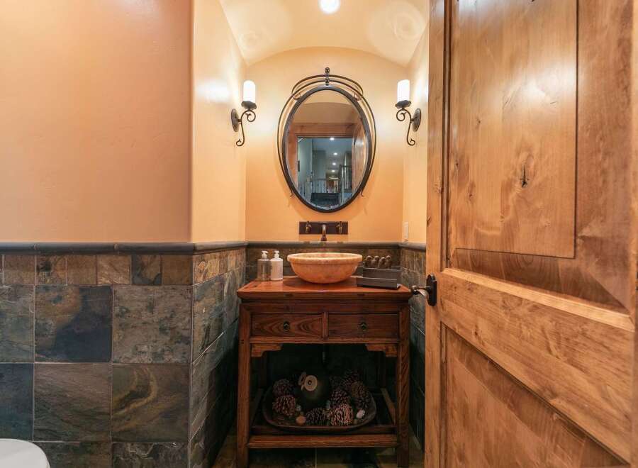 This powder room features a rustic wooden vanity with a stone vessel sink, complemented by slate tile wainscoting and warm, textured walls.