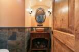 This powder room features a rustic wooden vanity with a stone vessel sink, complemented by slate tile wainscoting and warm, textured walls.