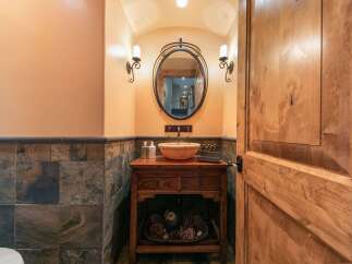 This powder room features a rustic wooden vanity with a stone vessel sink, complemented by slate tile wainscoting and warm, textured walls.