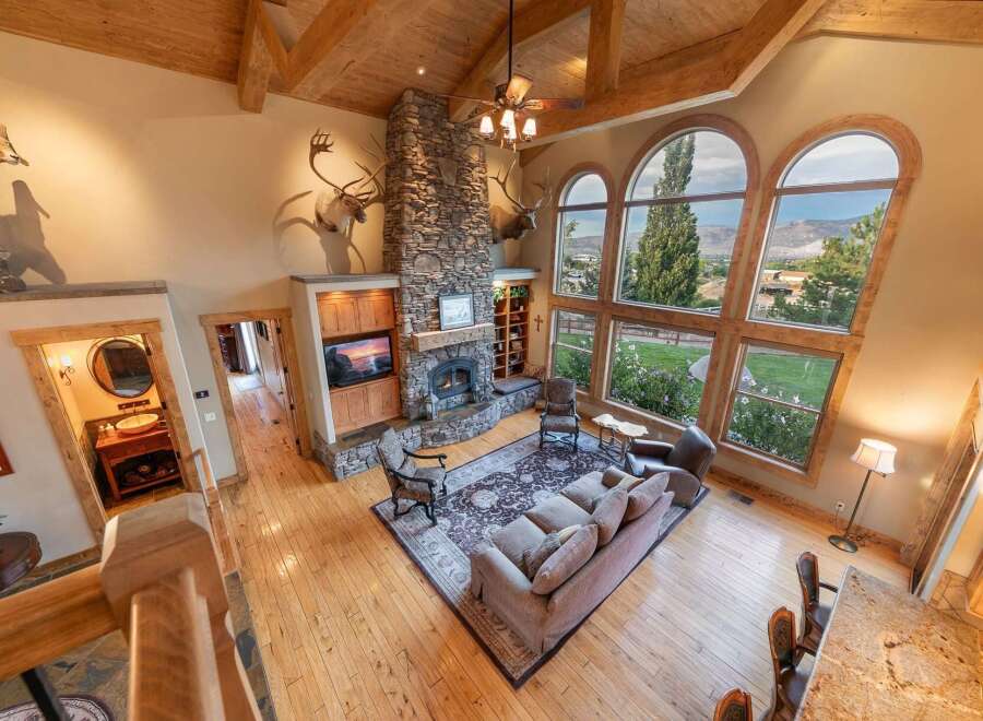 Experience breathtaking mountain views from this stunning living room, featuring a grand stone fireplace and soaring vaulted ceilings with exposed wooden beams.