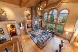 Experience breathtaking mountain views from this stunning living room, featuring a grand stone fireplace and soaring vaulted ceilings with exposed wooden beams.