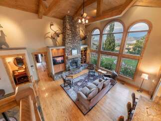 Experience breathtaking mountain views from this stunning living room, featuring a grand stone fireplace and soaring vaulted ceilings with exposed wooden beams.