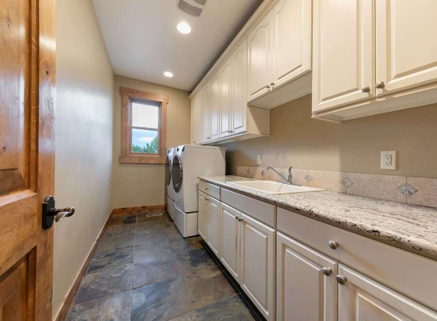 This spacious laundry room features a large sink, ample cabinet storage, and a granite countertop perfect for folding clothes.