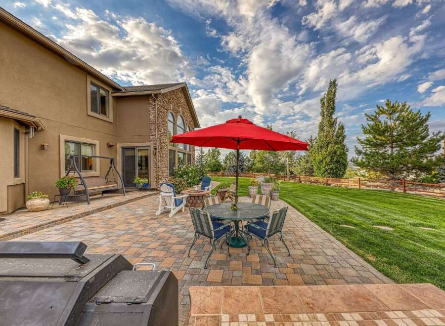 Enjoy outdoor living at its finest with this spacious patio featuring a dining set under a vibrant red umbrella, perfect for al fresco meals.