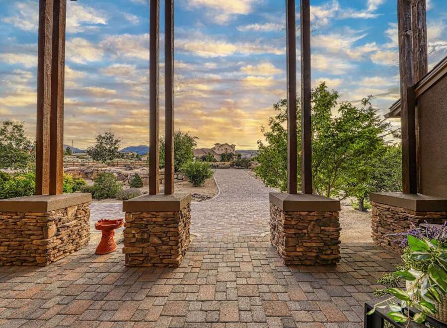 Experience breathtaking sunsets from this stunning property, framed by rustic stone pillars and a charming paver walkway leading to a magnificent home.