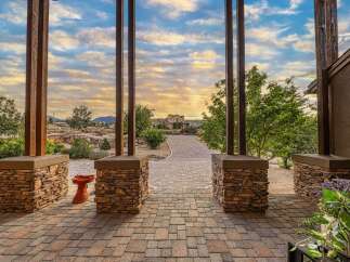 Experience breathtaking sunsets from this stunning property, framed by rustic stone pillars and a charming paver walkway leading to a magnificent home.