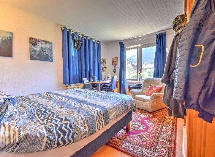 This cozy bedroom features a comfortable bed with a patterned duvet, a functional desk area, and a plush armchair perfect for relaxation.