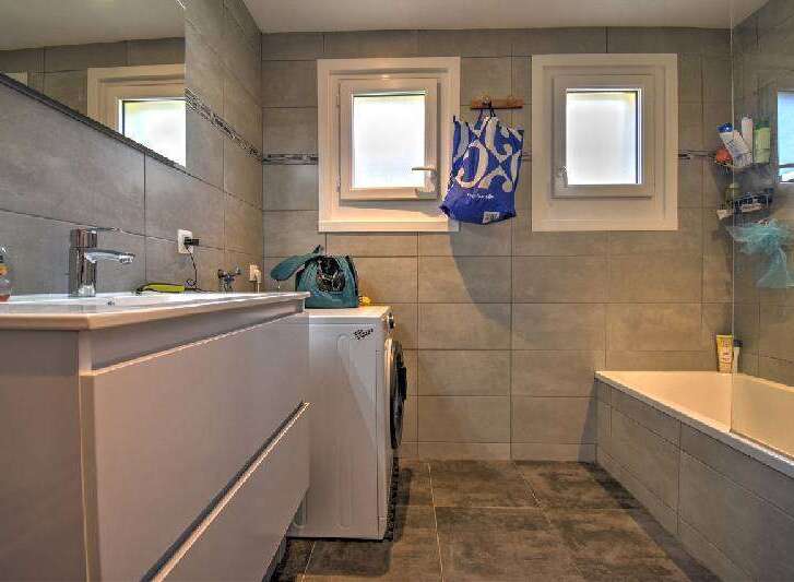 This modern bathroom features a sleek vanity with a built-in sink and ample storage, complemented by a matching washing machine.