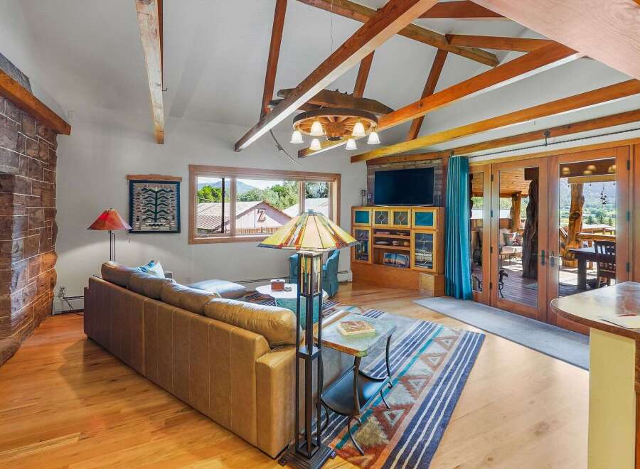 Experience rustic charm in this spacious living area featuring a soaring vaulted ceiling with exposed wooden beams and a unique wagon wheel chandelier.