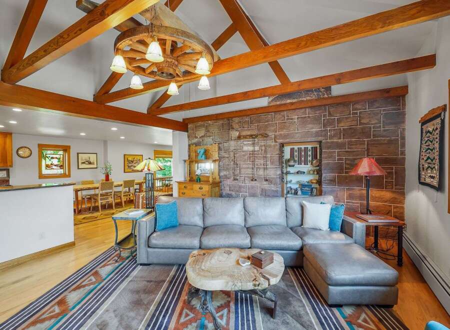 Experience rustic charm in this spacious living area, featuring a grand stone fireplace and exposed wooden beams that add warmth and character.