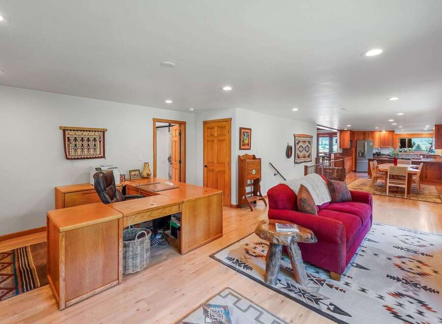 This spacious open-concept living area features a dedicated home office space with a large wooden desk and comfortable office chair.