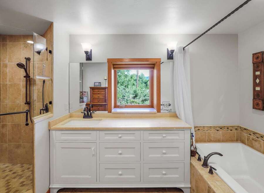 This spacious bathroom features a large vanity with ample storage and a bright window overlooking lush greenery.
