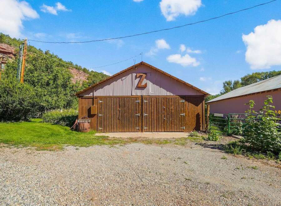 Discover this charming property featuring a rustic barn with large wooden doors, perfect for storage or housing animals.
