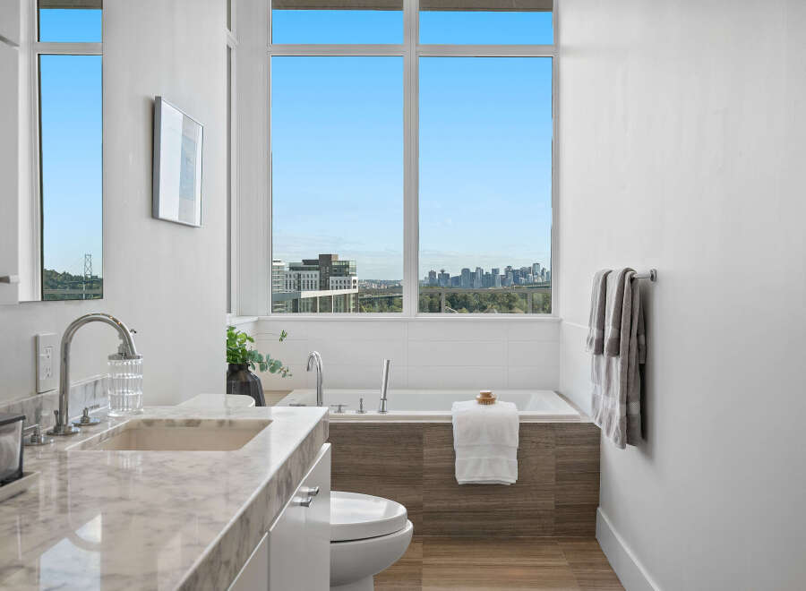 Experience luxury in this modern bathroom featuring a stunning marble vanity and a deep soaking tub with a breathtaking city view.
