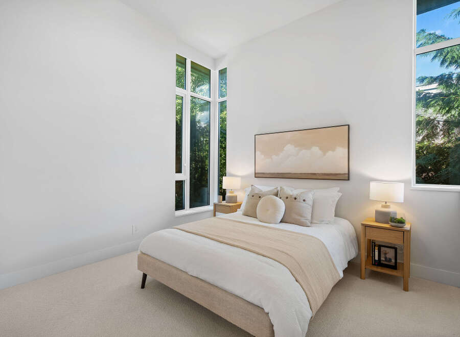 Experience modern living in this serene bedroom, featuring a plush bed adorned with decorative pillows and a neutral throw.