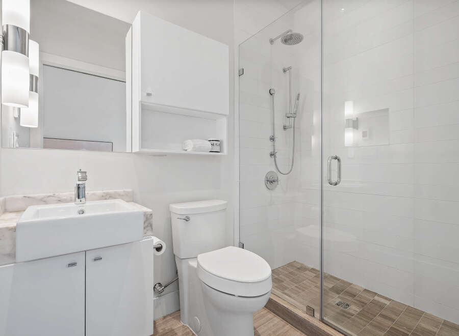 This modern bathroom features a sleek white vanity with a vessel sink and marble countertop, complemented by a matching toilet.