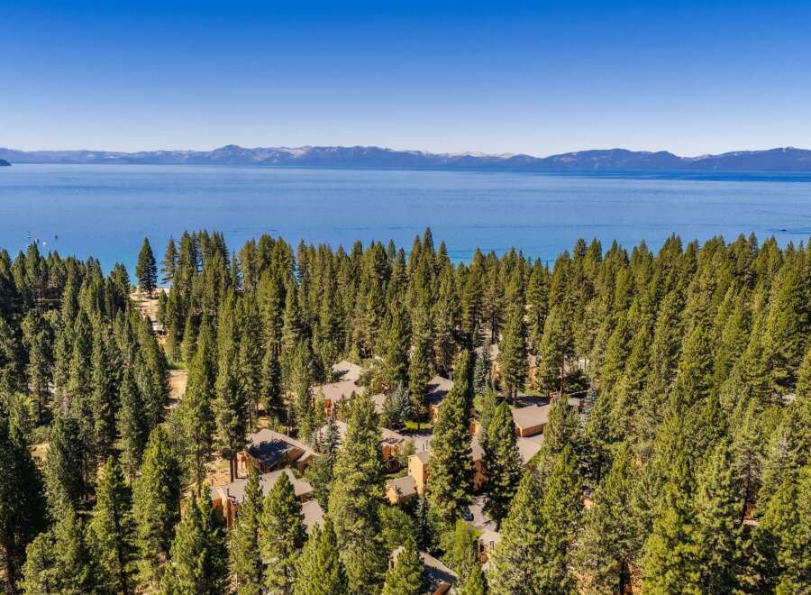 Nestled amidst a dense forest of pine trees, this property offers stunning panoramic views of a vast, blue lake and distant snow-capped mountains.