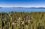 Nestled amidst a dense forest of pine trees, this property offers stunning panoramic views of a vast, blue lake and distant snow-capped mountains.