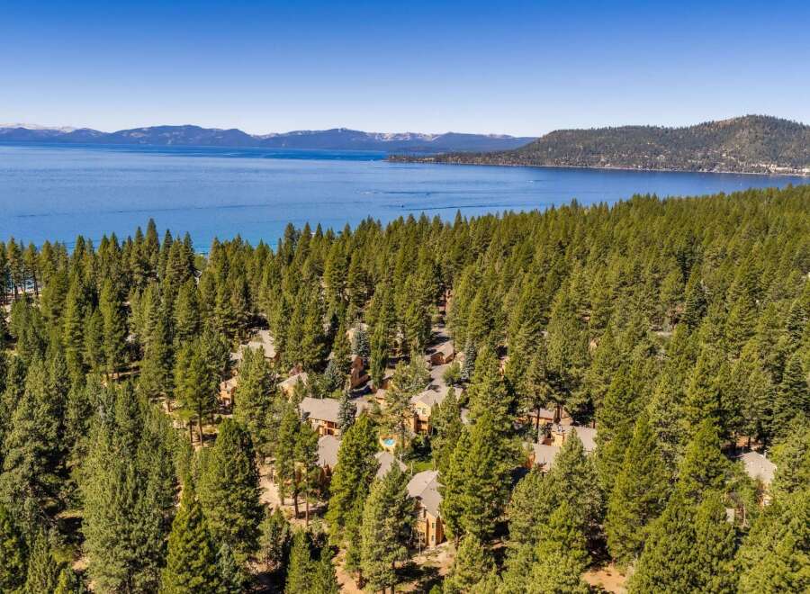 Nestled amidst a dense forest of evergreen trees, this property offers a serene retreat with stunning views of a vast blue lake and distant snow-capped mountains.