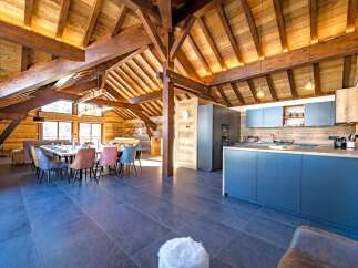 Experience luxury mountain living in this stunning open-plan chalet featuring a spacious dining area with a large wooden table and colorful upholstered chairs, perfect for gathering with loved ones.