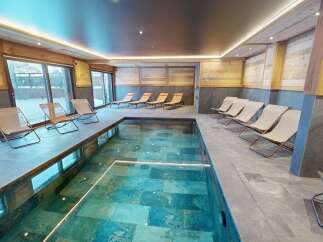 Experience ultimate relaxation in this luxurious indoor swimming pool area, featuring a stunning turquoise pool surrounded by natural wood accents and sleek stone tiling.