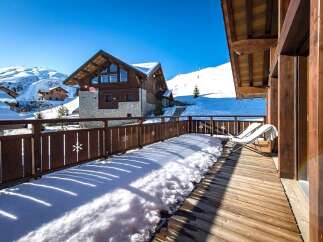 Experience the ultimate winter retreat in this stunning ski chalet, featuring a spacious wooden deck overlooking snow-covered mountains.