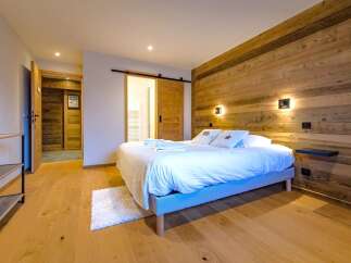 Experience rustic charm in this beautifully appointed bedroom, featuring a cozy bed with plush white linens and a striking wooden accent wall.