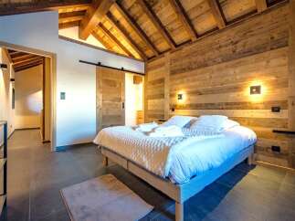 Experience rustic luxury in this charming bedroom, featuring a vaulted wooden beam ceiling and warm, wood-paneled walls.