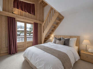 Experience cozy mountain living in this charming bedroom featuring a comfortable bed, warm wood paneling, and a private balcony with stunning snowy views.
