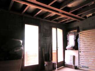 This unfinished attic space offers a blank canvas for renovation, featuring exposed wooden beams and ample natural light from double doors.