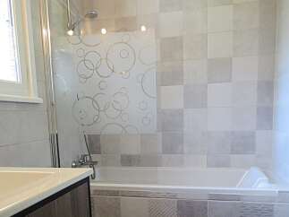 This modern bathroom features a sleek bathtub with a decorative frosted glass shower screen adorned with circles.