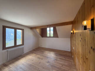 Experience breathtaking mountain views from this charming attic room, featuring a rustic wooden accent wall and exposed beams.