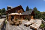 Enjoy al fresco dining on this expansive wooden deck, complete with a large outdoor dining table and chairs under a shaded umbrella.