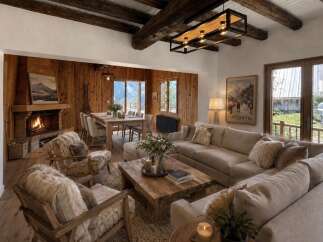 Experience rustic luxury in this stunning mountain lodge living room, featuring a grand stone fireplace and exposed wooden beams.