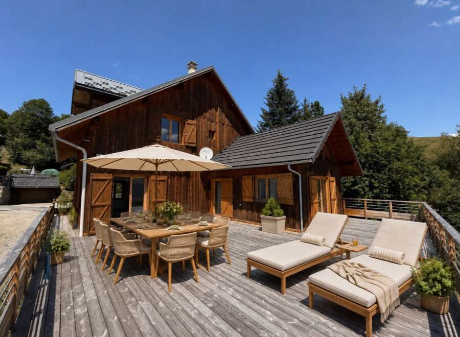 Enjoy al fresco dining on this expansive wooden deck, complete with a large outdoor dining table and chairs under a shaded umbrella.