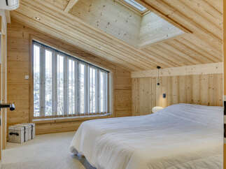 Experience cozy mountain living in this charming attic bedroom, featuring a sloped wooden ceiling and a large window offering scenic views.
