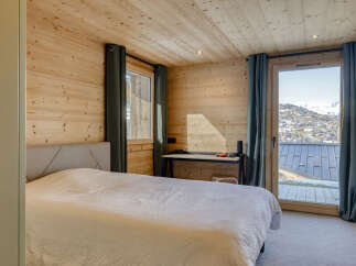 Experience breathtaking mountain views from this charming bedroom, featuring warm wood paneling and a comfortable bed.