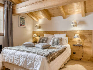 Experience cozy mountain living in this charming chalet bedroom, featuring exposed wooden beams and a plush queen-sized bed adorned with faux fur throws and decorative pillows.