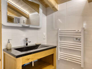 This modern bathroom features a sleek black sink set in a wooden vanity, complemented by a chrome faucet and a textured tile backsplash.