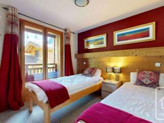 This charming bedroom features two twin beds with plush white bedding and vibrant red throws, perfect for a cozy mountain retreat.