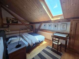 Discover this charming attic bedroom featuring a cozy bed with blue and white bedding, complemented by a skylight that floods the space with natural light.