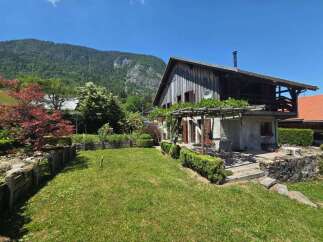 Charming rustic home nestled in a picturesque mountain setting, featuring a weathered wood exterior and a welcoming vine-covered pergola.