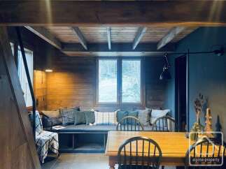 Experience cozy living in this charming wooden cabin, featuring a built-in bench with plush cushions and a large window offering scenic views.