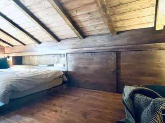 Experience rustic charm in this attic bedroom featuring a cozy bed and exposed wooden beams.