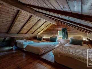 Experience rustic charm in this attic bedroom, featuring three cozy beds nestled under exposed wooden beams.