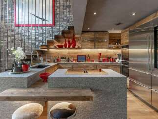 Experience luxury mountain living in this stunning kitchen featuring a unique stone island with a built-in cooktop and a rustic wooden breakfast bar.