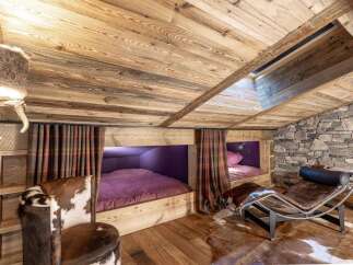 Experience rustic luxury in this charming mountain retreat, featuring cozy built-in bunk beds with plush purple bedding and plaid curtains.