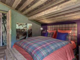 Experience rustic luxury in this charming bedroom, featuring a cozy plaid comforter and a striking abstract artwork.