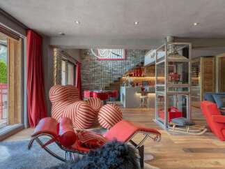 Experience luxury mountain living in this stunning chalet, featuring a vibrant red and white striped statement armchair and a sleek red chaise lounge.